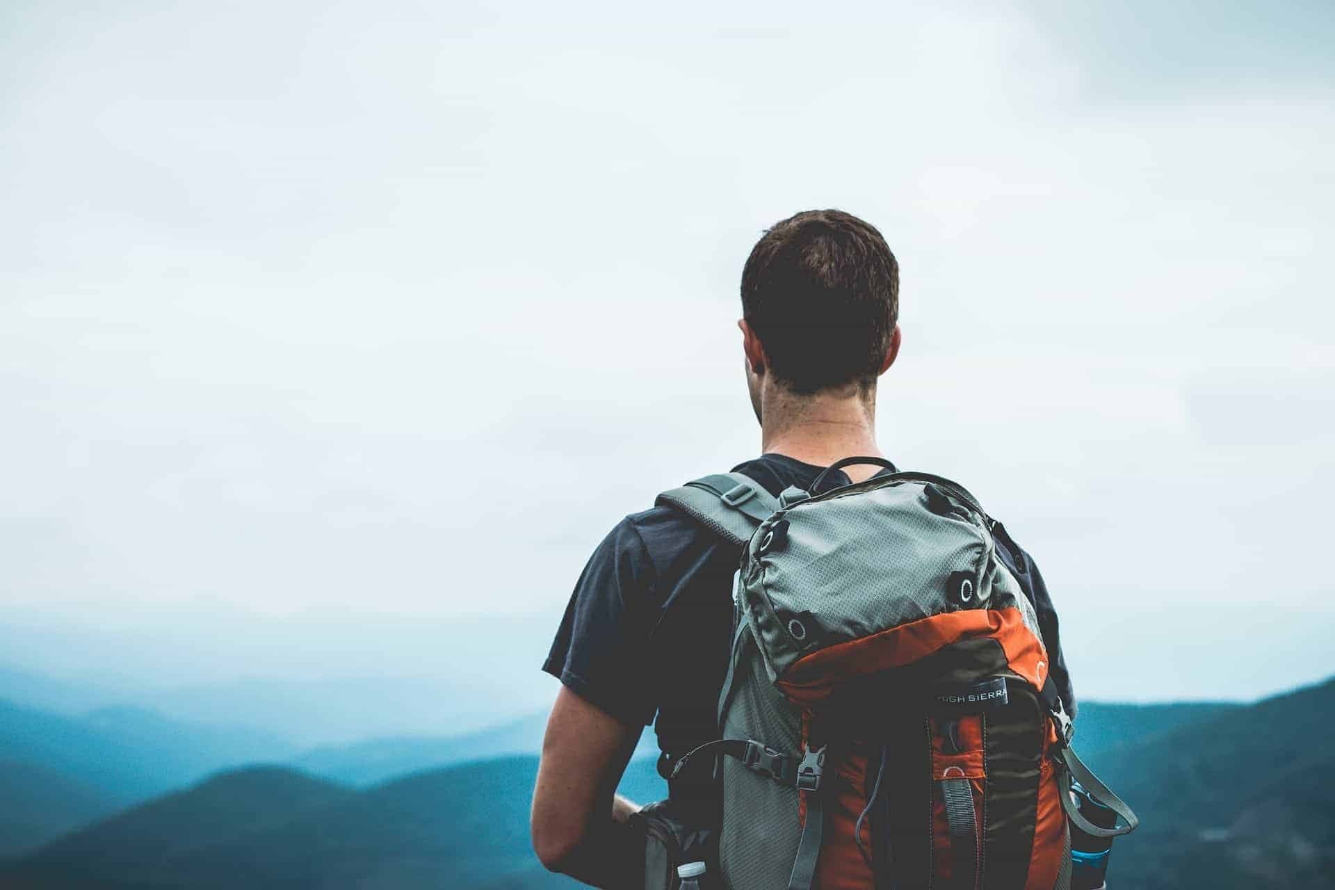 Man met een backpack staat boven op een berg.